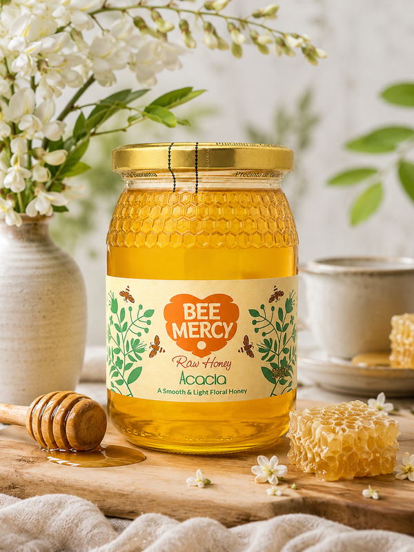 A glass jar of Bee Mercy Raw Honey Acacia centered on a wooden surface, surrounded by white flowers, a honey dipper, and a honeycomb piece in a softly styled setting.