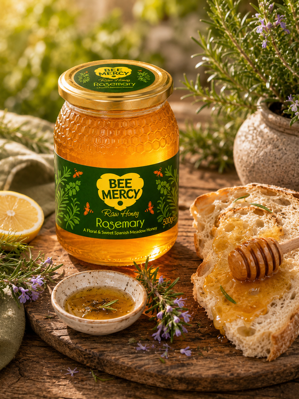 A jar of Bee Mercy Rosemary Honey sits on a rustic wooden board with slices of honeyed bread, a small dish of honey, lemon, and rosemary sprigs in a sunlit outdoor setting.