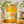 A glass jar of Bee Mercy Raw Honey Acacia centered on a wooden surface, surrounded by white flowers, a honey dipper, and a honeycomb piece in a softly styled setting.