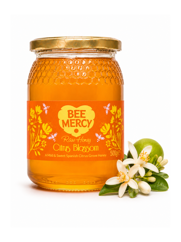 A 500g glass jar of Bee Mercy Raw Honey Citrus Blossom on a white background, styled with a green lime and white citrus blossoms.