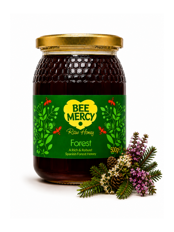 A 500g glass jar of Bee Mercy Forest Raw Honey with a gold lid and green label, styled with natural forest herbs and a pinecone on a white background.