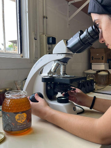 Person using a microscope with a jar of honey on a lab counter