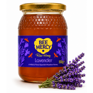 A 500g glass jar of Bee Mercy Lavender Raw Honey with a gold lid and a purple label, styled with a bouquet of fresh lavender sprigs on a white background.