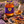 A jar of Bee Mercy Lavender Raw Honey displayed on a rustic wooden table with a plate of honey toast topped with figs and lavender, alongside a honey dipper, blueberries, and a vase of lavender in a warm, sunlit outdoor setting.