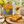 A jar of BEE MERCY Raw Honey Mountain honey sits on a rustic wooden table next to a plate of toast with honey dripping from a wooden dipper, with flowers and a mug in the background.