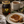A jar of Bee Mercy Rose Honey Oak on a rustic wooden table next to a cup of tea, a slice of bread with honey on a plate, and an acorn.