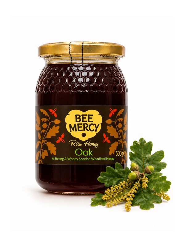 A 500g glass jar of Bee Mercy Raw Honey Oak flavor with a gold lid and a black label with yellow and orange accents, shown next to fresh green oak leaves and acorns on a white background.