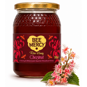 A 500g glass jar of Bee Mercy Raw Honey Chestnut, filled with deep reddish-brown honey and topped with a gold lid, shown next to pink and white chestnut blossom flowers on a white background.