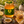 A jar of Bee Mercy Rosemary Honey sits on a rustic wooden board with slices of honeyed bread, a small dish of honey, lemon, and rosemary sprigs in a sunlit outdoor setting.