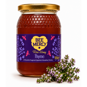 A 500g glass jar of Bee Mercy Raw Honey Thyme on a white background, styled with a small sprig of fresh thyme in front of the label.